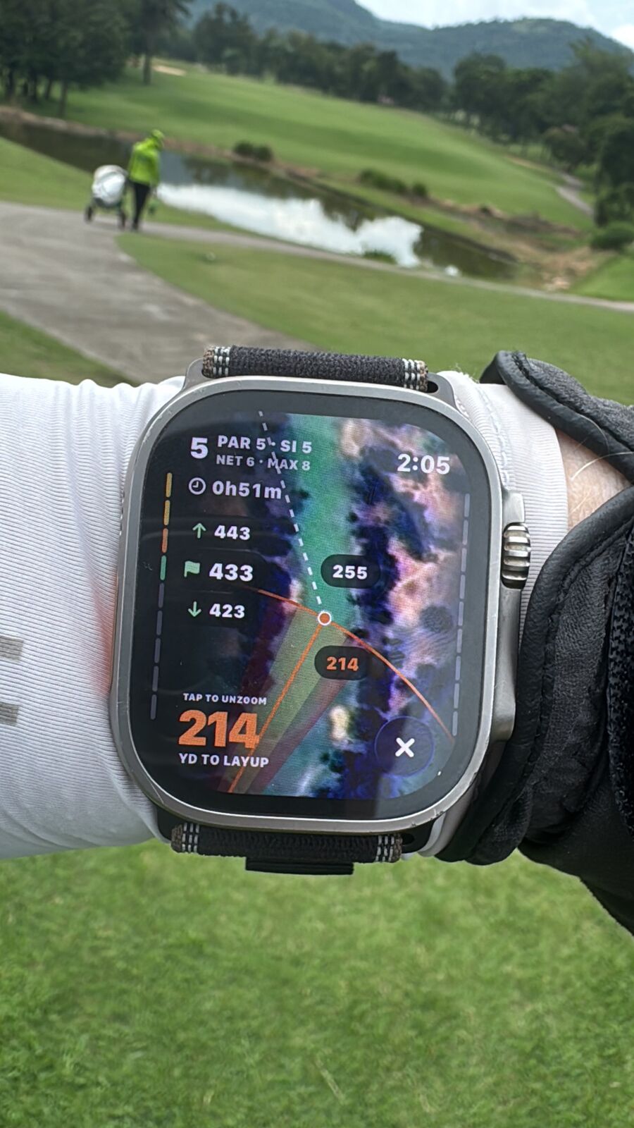 An Apple Watch on a golfer's wrist during a round: hole 5, par 5, 214 yards to the layup, the fairway and a pond behind